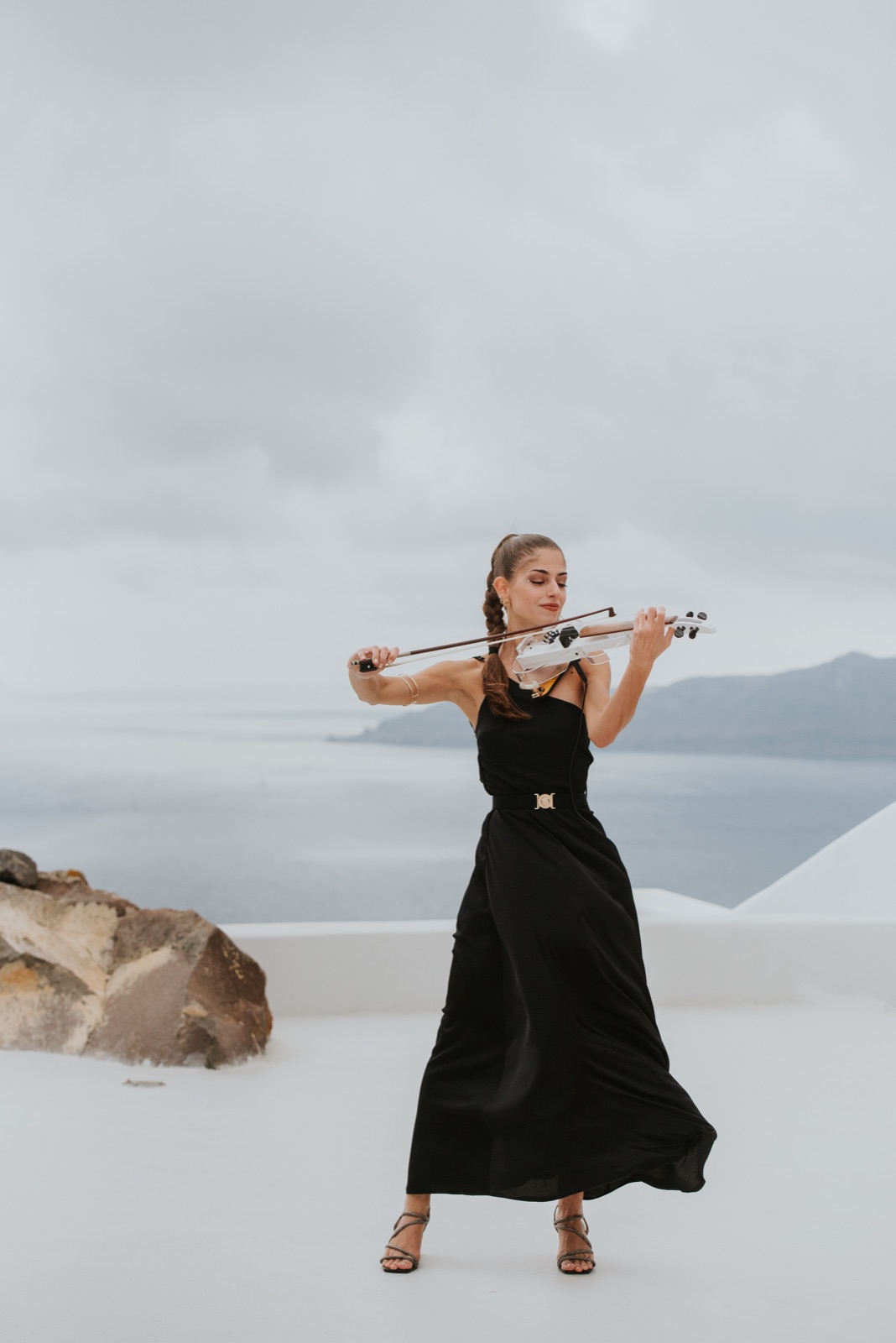 Marvi performing in a black gown on a Santorini cliff terrace